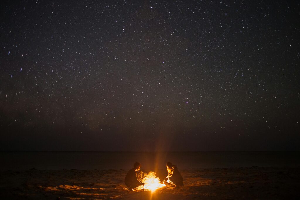 Unrecognizable couple near bonfire on coast at night sky